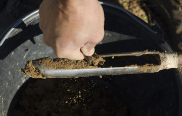 Prélèvement de terre : des mains vident la gouge de la tarière dans le seau début 2026 en Bretagne